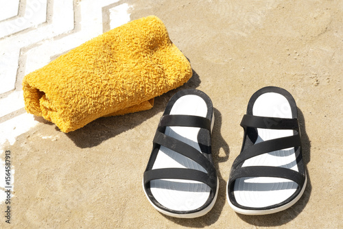 Black sandals and a yellow towel resting on sandy beach during a sunny day