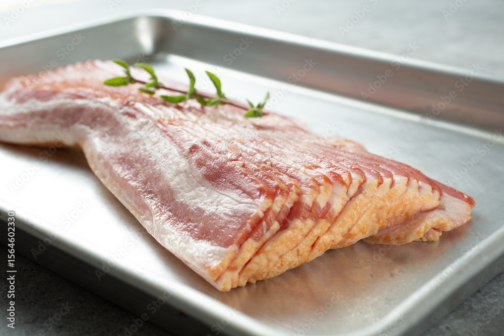 A closeup view of a stack of raw bacon on a baking sheet. A closeup view of a stack of raw bacon on a baking sheet.