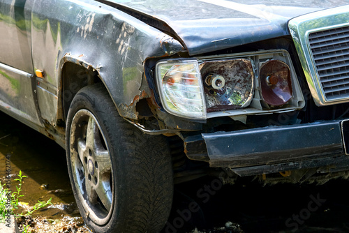 Old car with a rusty wing, a broken headlight and a flat tire