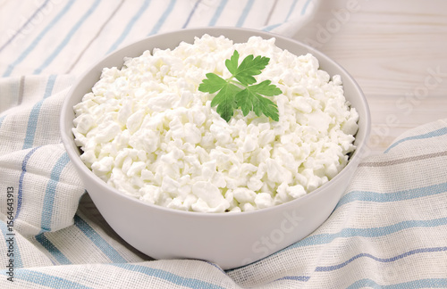 Farm cheese in a bowl on a light wooden background. Cottage cheese with parsley.