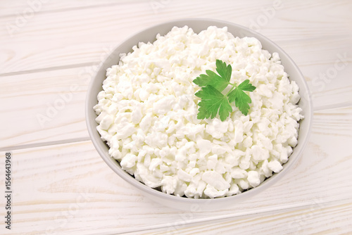 Farm cheese in a bowl on a light wooden background. Cottage cheese with parsley.