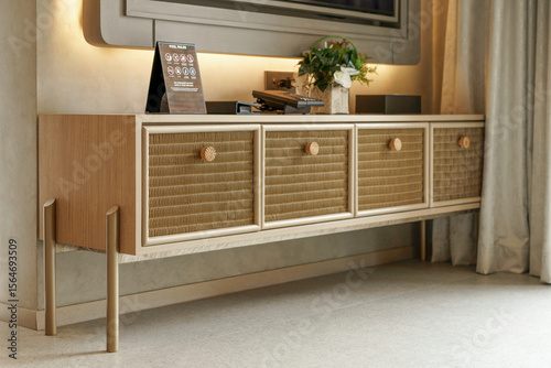 Modern wooden media console or TV stand with woven rattan drawers and matching knobs. Japandi style furniture in a contemporary living room with soft ambient lighting in the background.