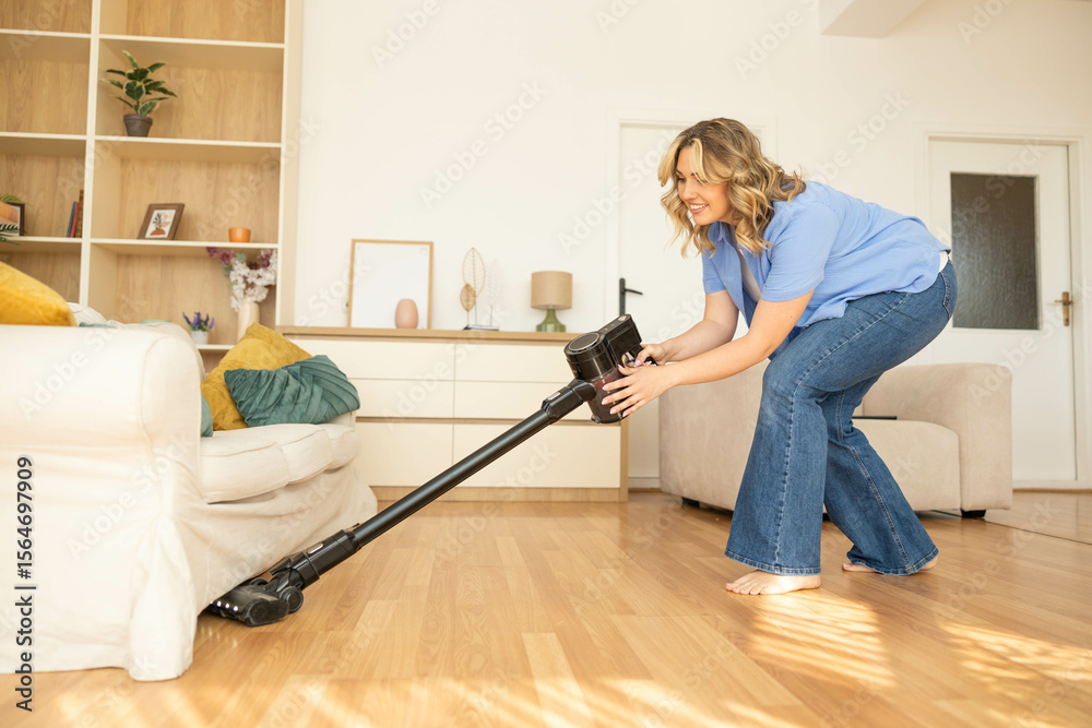 Fototapeta premium A woman is actively vacuuming the living room, ensuring cleanliness of her home while enjoying the task in a cozy setting.
