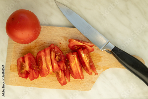 sliced tomato and kitchen knife on cutting board for Hungarian lecsó