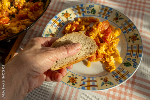 hand holding bread slice above plate of Hungarian lecsó