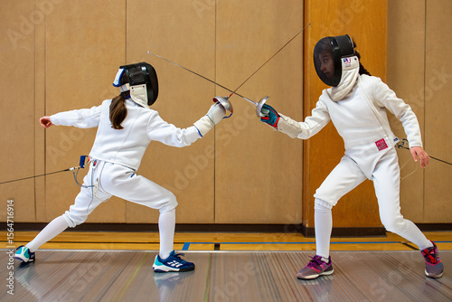 Two fencers in white gear lunge toward each other during an intense bout on an indoor fencing piste.