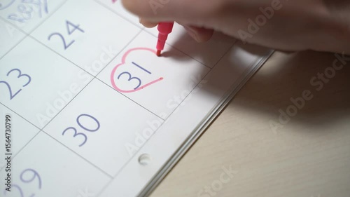 Female hand marking dates on calendar planning birth control
