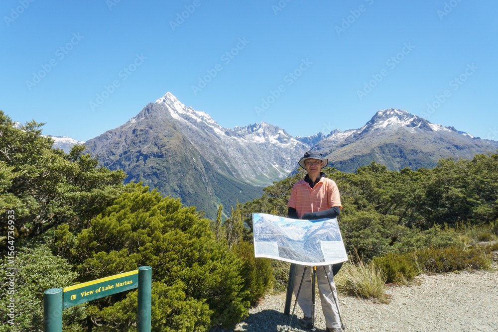 Naklejka premium Tourist posing for photos at the information board at Key Summit. Routeburn Track. South Island.