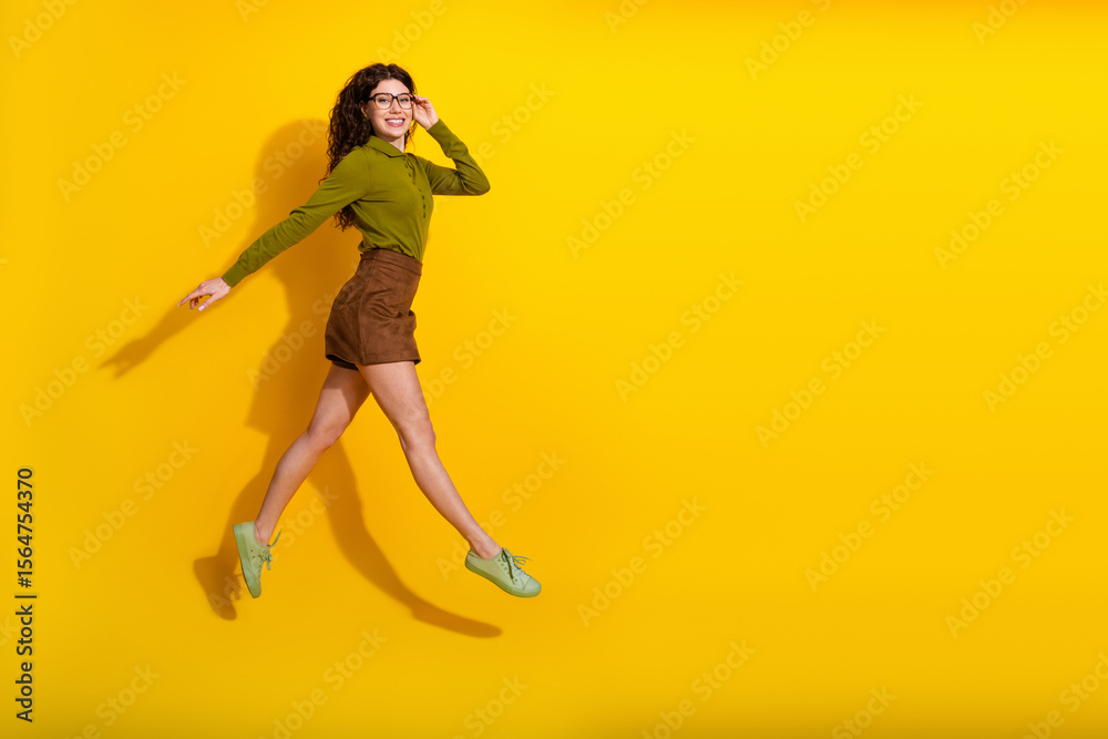Stylish young brunette woman jumping joyfully against a vibrant yellow background showcasing casual trendy fashion attire Stylish young brunette woman jumping joyfully against a vibrant yellow background showcasing casual trendy fashion attire
