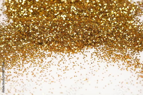 A sparkling close-up of loose gold glitter, piled at the top and scattered across a light surface, creating a festive background
