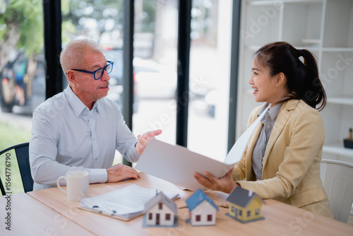 Real estate agent engaging with a customer in an office setting, discussing contract details while presenting house models and project plans, fostering a productive business dialogue