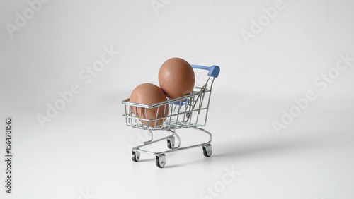 Photos Two fresh brown eggs are in a small model cart on a white background