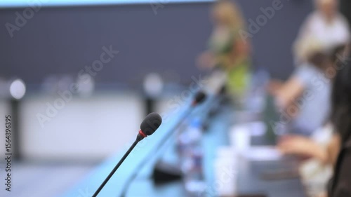 Microphone is on a table in front of a group of people. The microphone is black and red