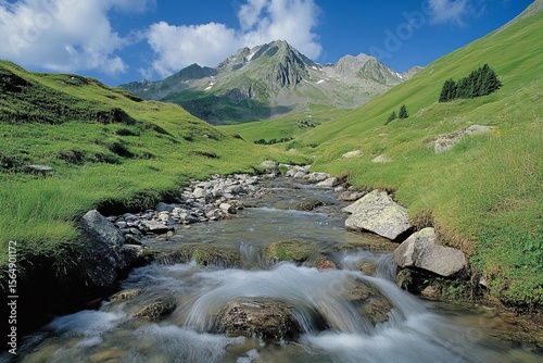 Majestic alpine mountain landscape with clear river stream flowing over rocks and green meadows under blue sky