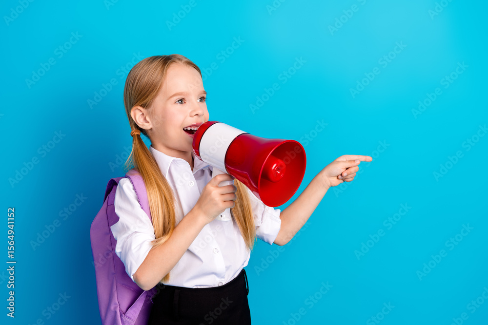 Excited schoolgirl using a red megaphone while pointing against a blue background expressing enthusiasm and energy Excited schoolgirl using a red megaphone while pointing against a blue background expressing enthusiasm and energy