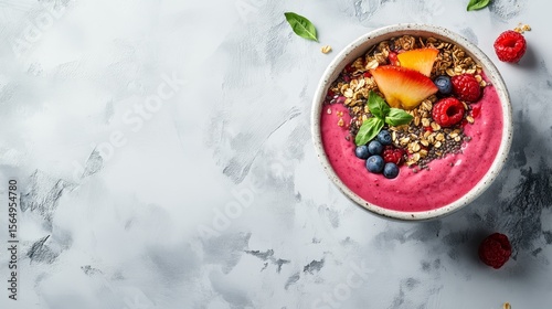 Top-down view of a vibrant smoothie bowl with granola, chia seed, and fresh fruit, symbolizing healthy eating, nutritious breakfast, and a balanced lifestyle on a textured gray background