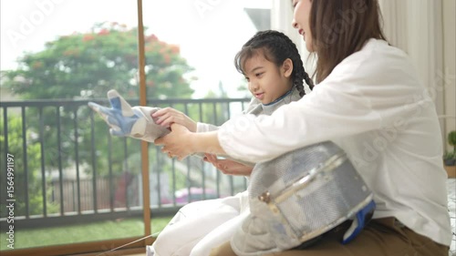 A girl in fencing gear with their mother preparing sports equipment before practicing fencing in preparation for the upcoming competition day