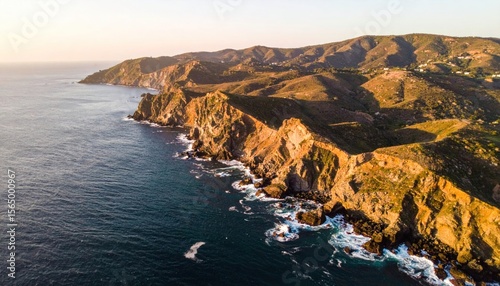 Aerial view of jagged cliffs meeting blue ocean under golden hour sunlight