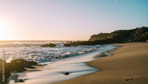 Sunny shore with rocks, waves, and sand leading to a distant headland under a clear sky
