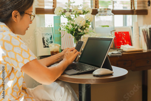 Business woman hands using cell phone while working on laptop.