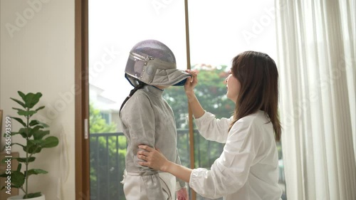 A girl in fencing gear with their mother preparing sports equipment before practicing fencing in preparation for the upcoming competition day
