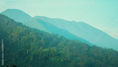 Layered mountain landscape with lush green forests and distant blue peaks under a serene sky, showcasing atmospheric perspective.