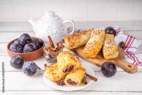 Vertuta, homemade strudel hand pies with sweet plum jam and spicy filling, with cinnamon, on a wooden kitchen background with juicy dark plums and spices