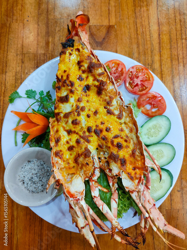 Whole grilled lobster with cheese and garlic, served with vegetables, pepper and salt. Restaurant in Nha Trang, Vietnam. Selective focus, close-up, top view.