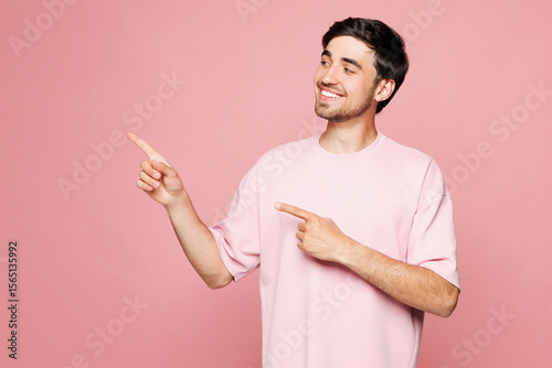 Young smiling happy Caucasian man he wear t-shirt casual clothes pointing index finer aside indicate on workspace area isolated on plain pastel light pink background studio portrait Lifestyle concept