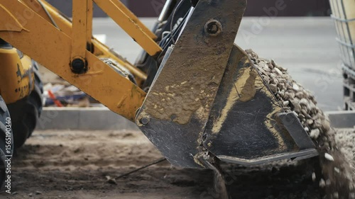An excavator is vigorously scooping gravel soil at a busy worksite, showcasing various construction machinery in action