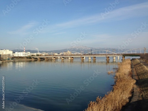 Fotografie A scenic view of a city, a truss bridge crossing the Kiso River, and the snow-capped Mount Ibuki in the distance in Japan