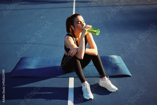 Fototapeta Naklejka Na Ścianę i Meble -  Sportswoman drinking water after training on fitness mat outdoors