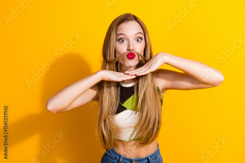 Photos Playful young woman making a mustache with her hair against a bright yellow background, expressing joy, laughter, and unique charm