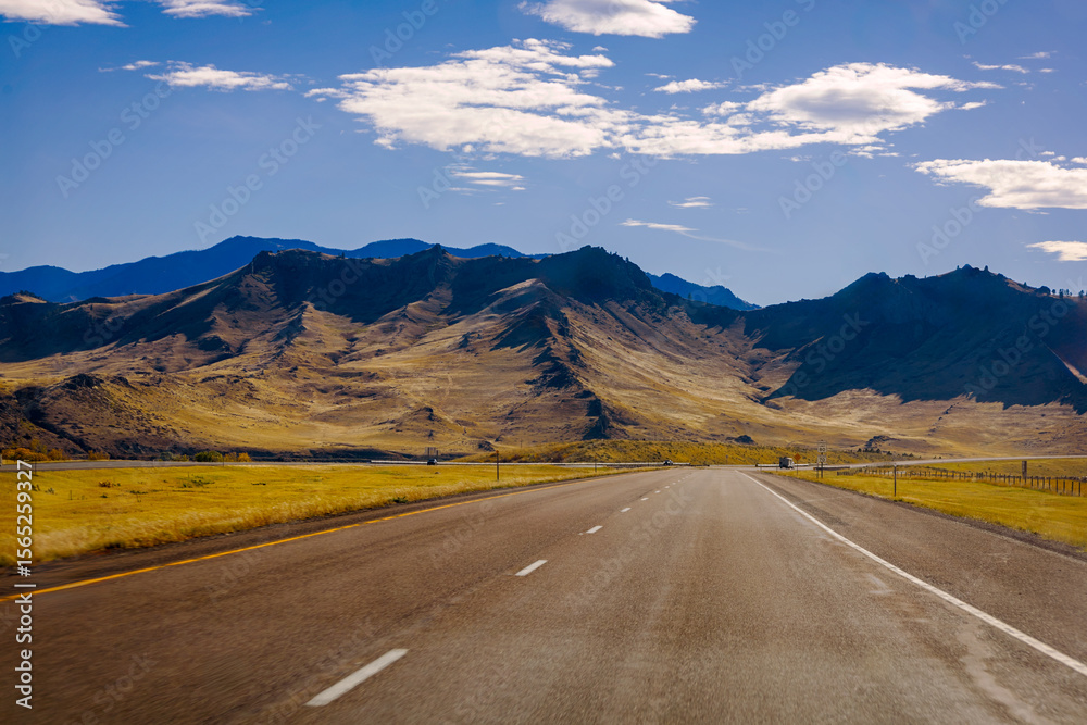 Fototapeta premium Driving through Montana on an empty highway under a cloudy sky
