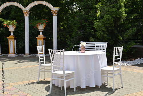 A beautiful restaurant with round tables covered in white tablecloths and surrounded by chairs, set up outdoors for a festive celebration