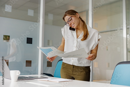 A dedicated professional woman is reviewing important paperwork while simultaneously multitasking on a phone call