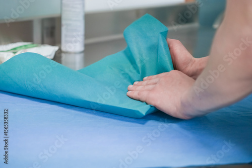 Close-up shows hands carefully folding blue-green medical fabric for sterilization, emphasizing infection control and patient safety within a healthcare environment, with ample copy space