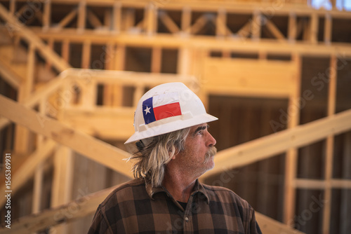 Construction Worker Wearing Hard Hat with Texas Flag Sticker Walking Inside Wooden Frame of House at Construction Site