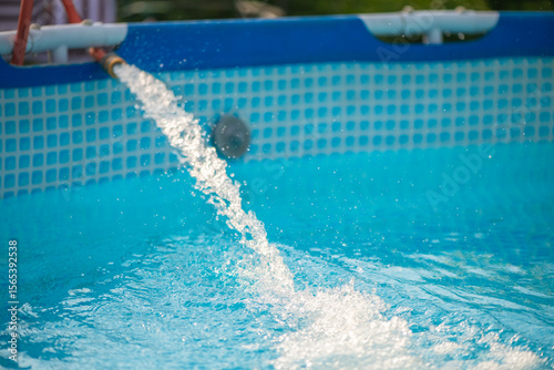 Crystal clear fresh water is being poured into a home garden pool from a garden hose on a sunny summer day, providing a refreshing escape from the heat