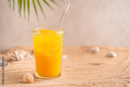 Fototapeta Naklejka Na Ścianę i Meble -  Colourful orange cocktail in a tall glass on a sand of a golden beach at a tropical holiday resort background an enjoyable summer vacation. High quality photo