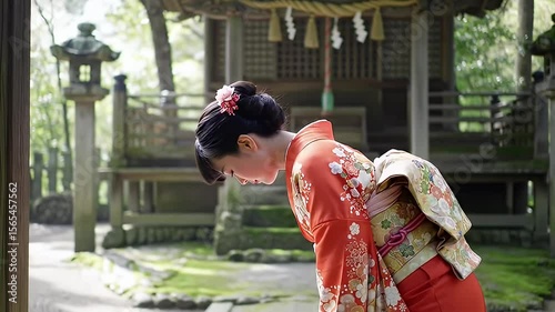 Japanese woman bows in traditional kimono before an aged shrine in a green garden