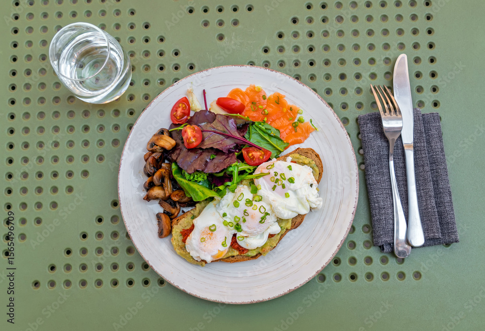 Gourmet breakfast plate with poached eggs on avocado toast, smoked salmon, and fresh salad.Top view.Healthy and balanced brunch with avocado toast, poached eggs, smoked salmon, and side of mushrooms Gourmet breakfast plate with poached eggs on avocado toast, smoked salmon, and fresh salad.Top view.Healthy and balanced brunch with avocado toast, poached eggs, smoked salmon, and side of mushrooms
