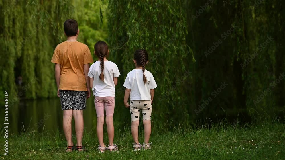 Three Young Children Stand Together, Backs to Camera, Observing the Serene Green Nature Park. Three Young Children Stand Together, Backs to Camera, Observing the Serene Green Nature Park.