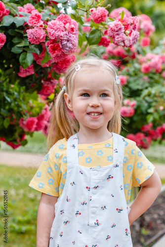 Child girl in a blooming garden with bushes of roses and flowers