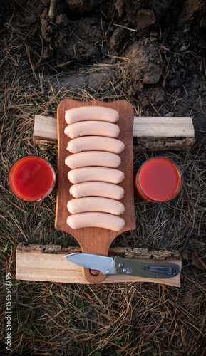 Outdoor Picnic Preparation: Sausages, Juice, and Knife on a Wooden Board in the Forest