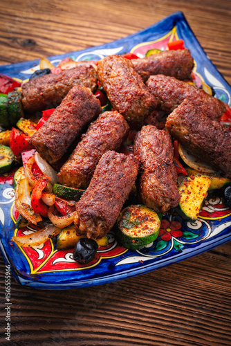 Traditional Croatian cevapi spicy meat ball rolls with troasted vegetables served as close-up on rustic design plate