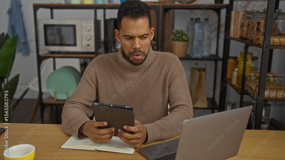 Young hispanic man in office with laptop, tablet, and notebook concentrating on work in a modern, organized interior room. Young hispanic man in office with laptop, tablet, and notebook concentrating on work in a modern, organized interior room.