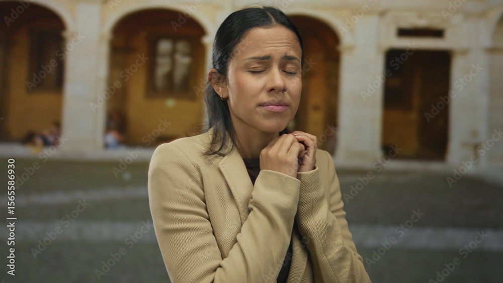 Fototapeta premium Woman in jacket looks worried in historic town square with arches in background, conveying emotion and narrative against old architecture.