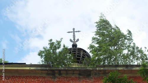Crumbling dome of church, which has an onion-shaped design and Orthodox cross at top, is located on top of brick building that has now grown over with vegetation.