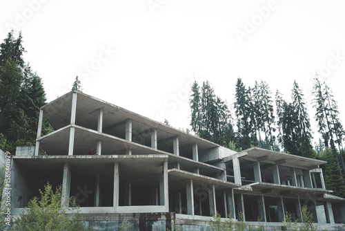 Wallpaper Mural Abandoned concrete building under construction surrounded by pine forest. Unfinished multi-storey structure with columns and slabs against cloudy sky Torontodigital.ca